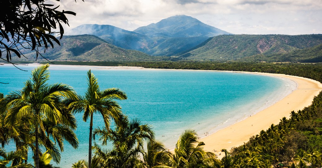 Port Douglas Queensland Australia October 7 2018: Trinity Bay Lookout. Beautiful tropical beach with smoke from bush fire burning in the hills behind. Palm trees, clean beach sand with people swimming