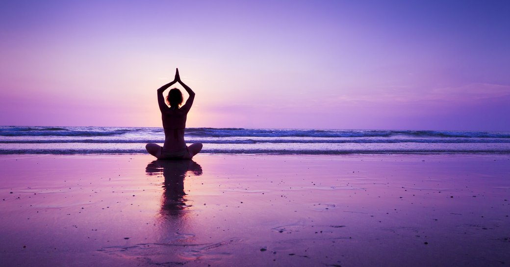 someone doing a yoga pose on a beach in thailand silhouetted against a purple sky